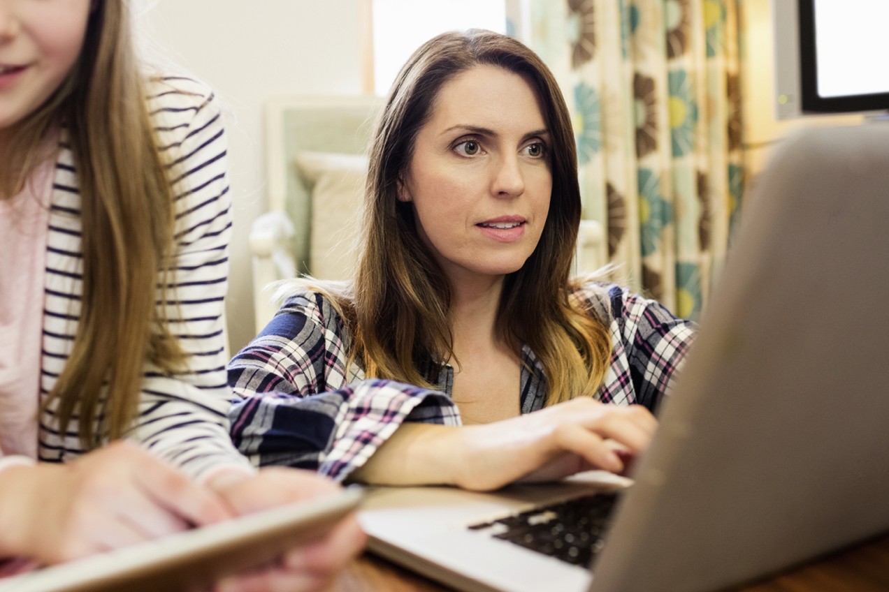 Frau am Laptop, Teenager im Hintergrund erkennbar