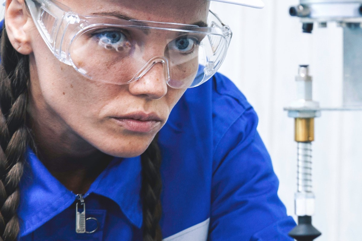 Eine junge Wissenschaftlerin in Schutzkleidung an einer Maschine.