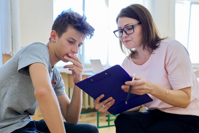 Ein Junge und eine Frau sitzen nebeneinander und schauen auf ein Klemmbrett