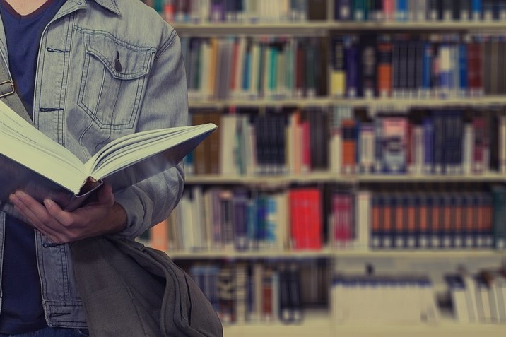 Mann mit Buch in der Hand steht vor einem großen Bücherregal