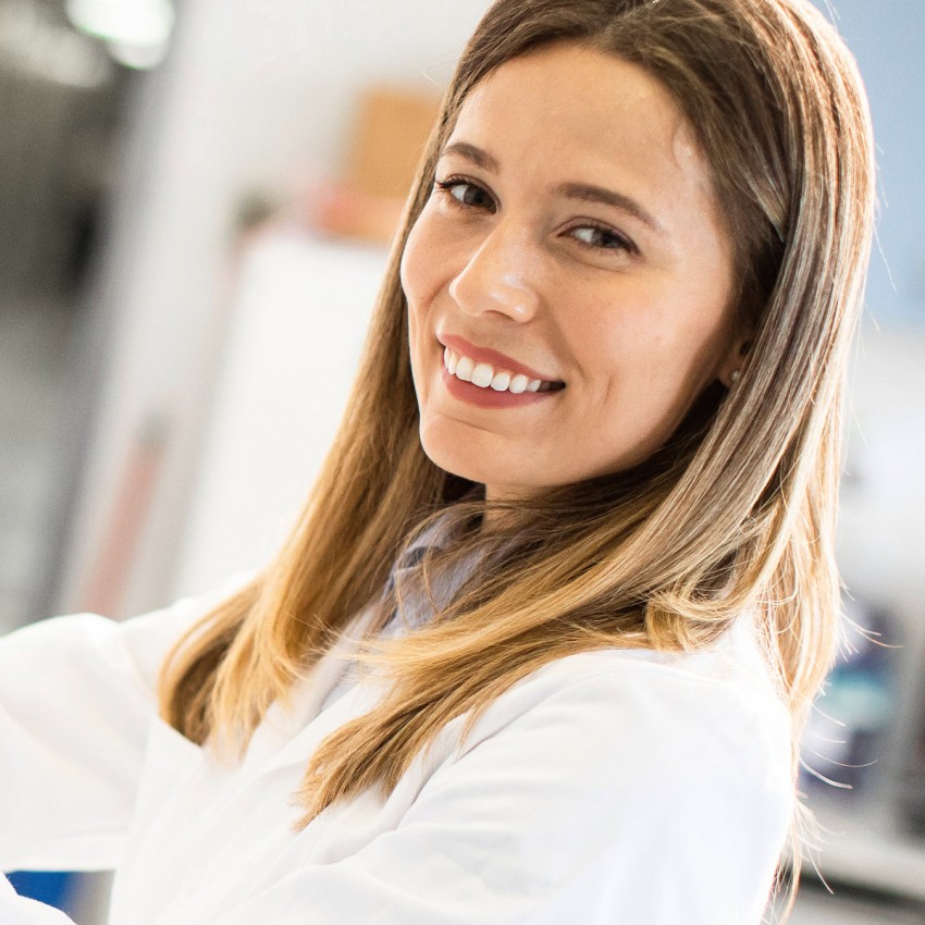 Ein lächelnde junge Wissenschaftlerin im weißen Kittel.
