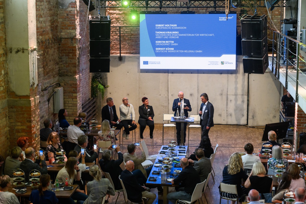 Vogelperspektive auf eine Podiumsdiskussion und davor viele sitzende Menschen
