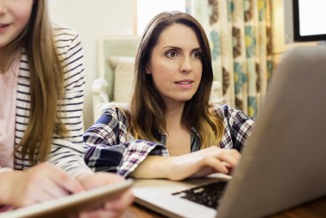Frau am Laptop, Teenager im Hintergrund erkennbar