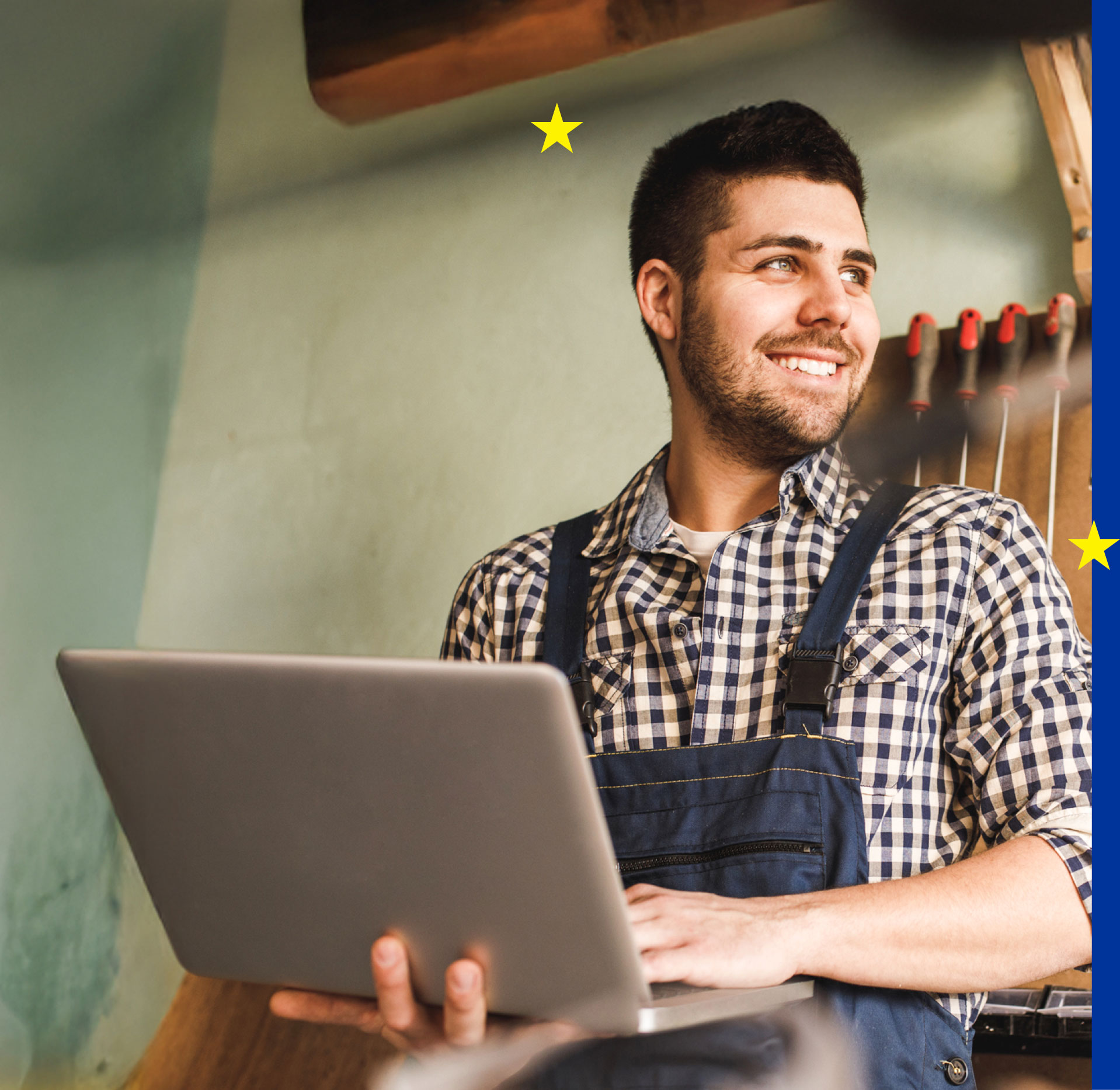 Mann mit Latzhose im Handwerksbetrieb am Laptop